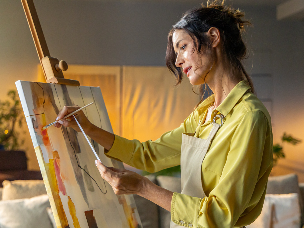 Mlada djevojka, tamne kose skupljenje u punđi, slika na platnu vodenim bojama.