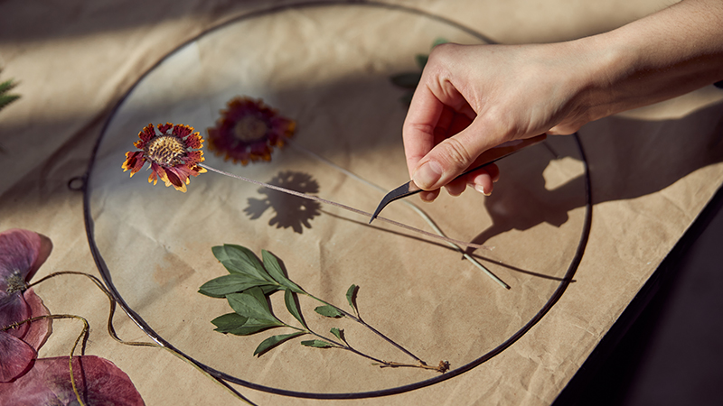 Na smeđem papiru se radi aranžman od suhog cvijeća i listova. Osoba ih slaže pincetom.