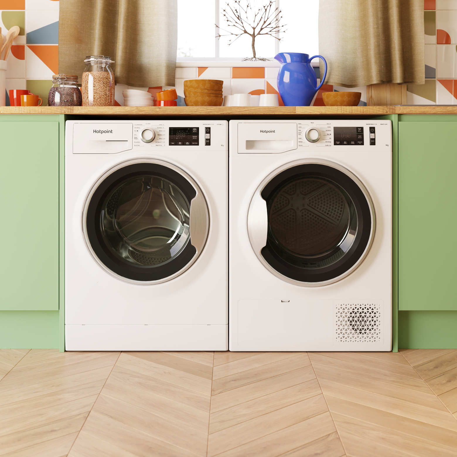 Pair of white Hotpoint washing machine and tumble dryer in a modern kitchen with green cabinets in a straight shot