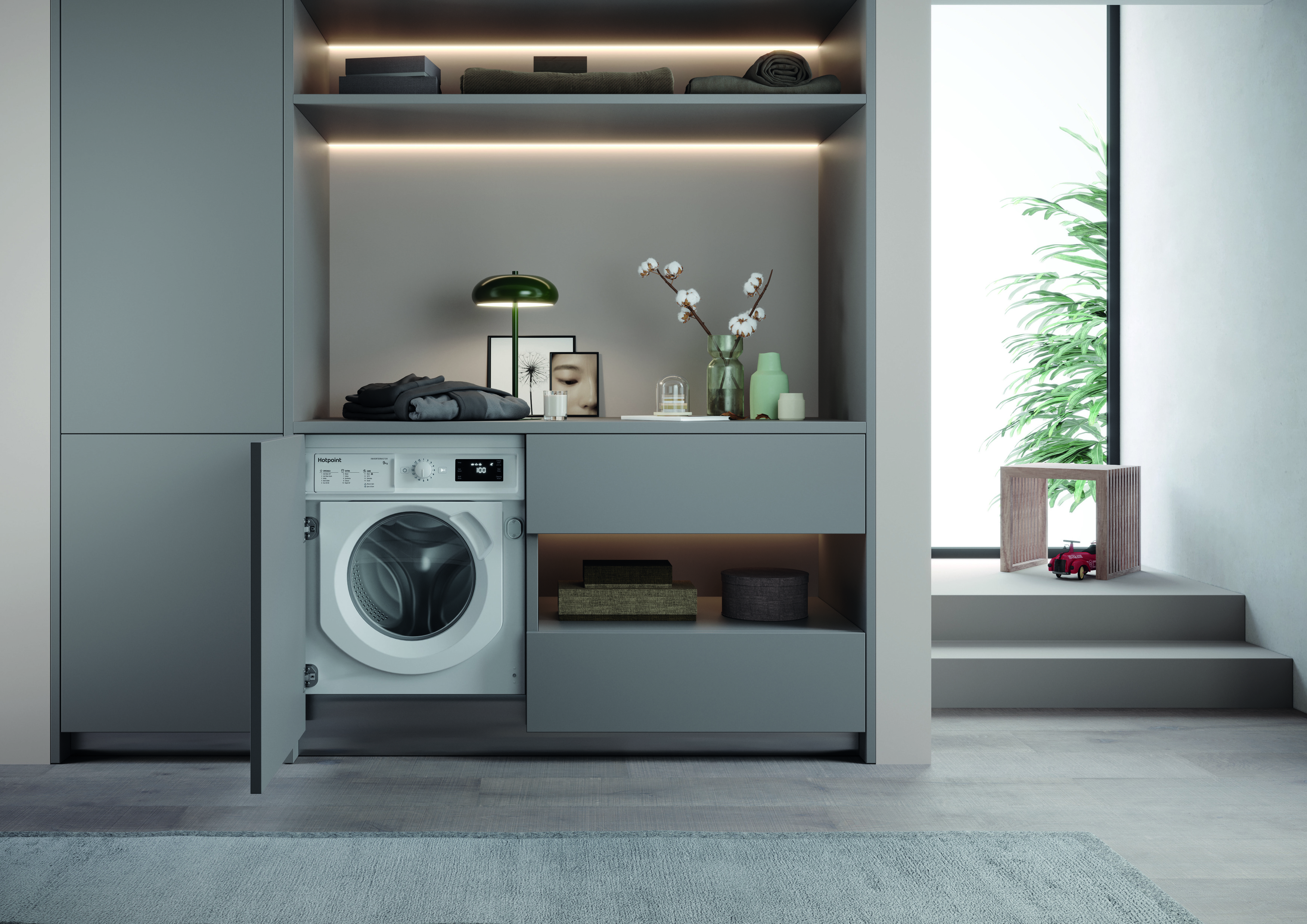 A modern, minimalist laundry room featuring a white washing machine partially integrated into a custom cabinet, with open shelves, a potted plant, and decorative items against a neutral backdrop.