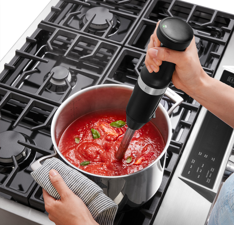 Black hand blender mixing tomato sauce