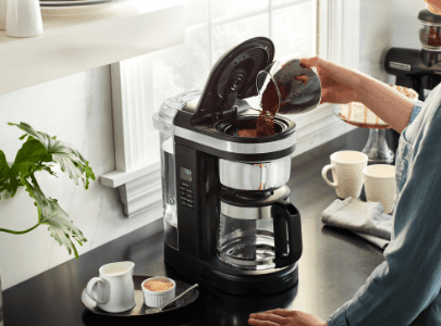 Black drip coffee maker being filled with coffee