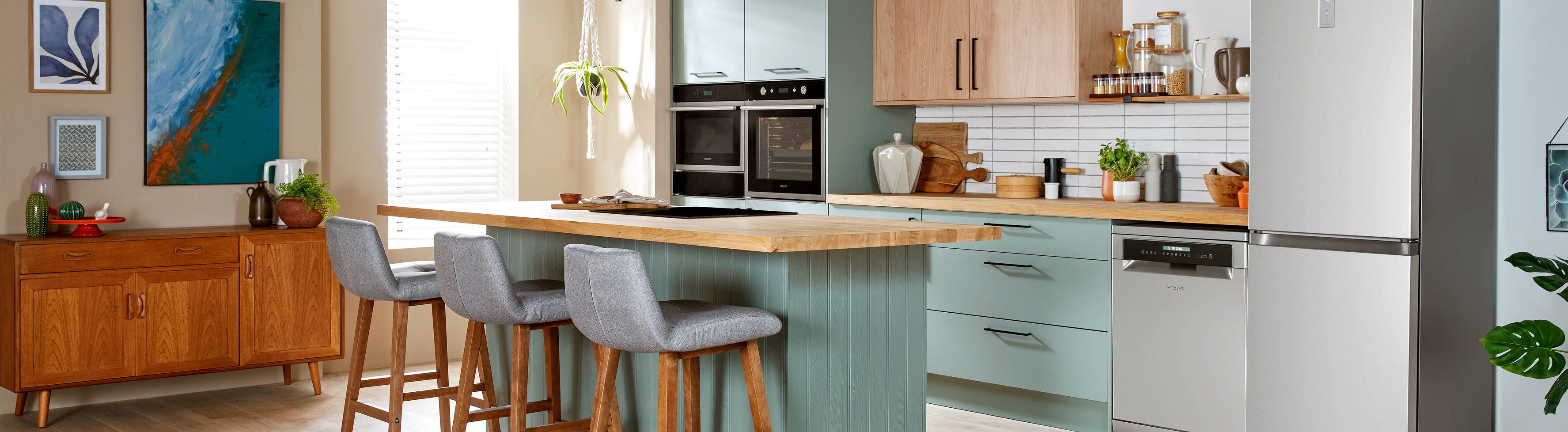 A modern kitchen featuring light teal cabinets, wood countertops, stainless steel appliances, and bar stools at a kitchen island.