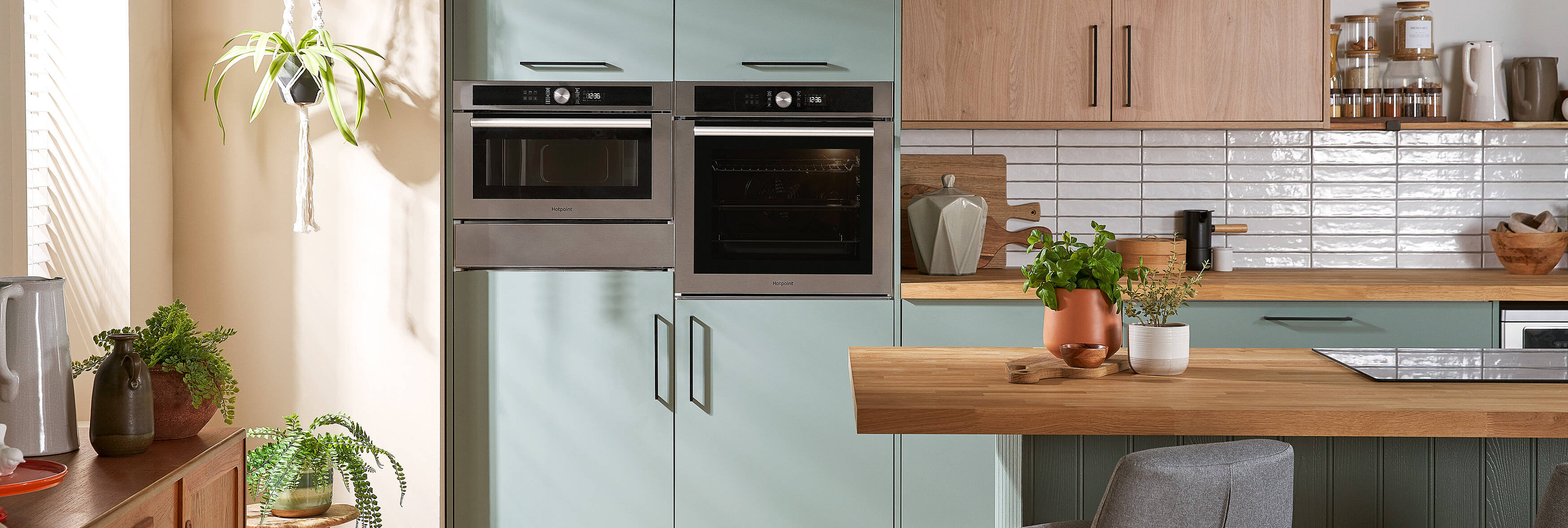 A woman is removing a tray with a cooked chicken and vegetables from a built-in oven in a modern kitchen.