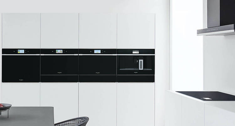 Bijela kuhinja s crnim uređajima, pećnicama, pločom, napom i ugradbenim kave-aparatom koji se savršeno uklapa u ovu modernu minimalističku kuhinju.