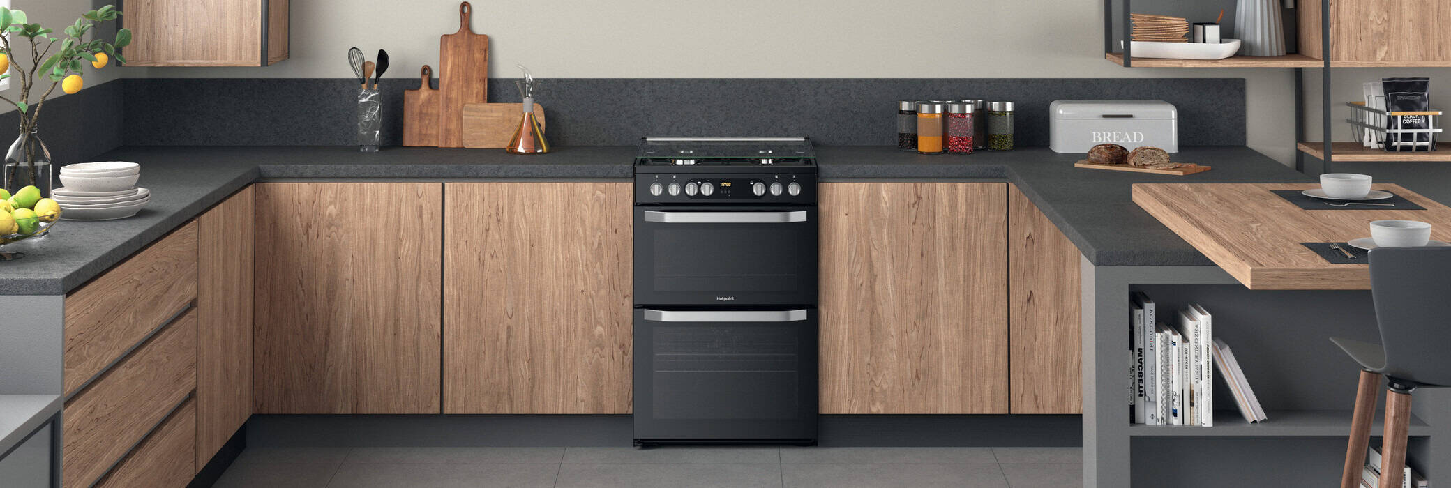 A modern kitchen with wood cabinets, dark countertops, a black oven, cutting boards, jars, and a small breakfast bar with a chair.