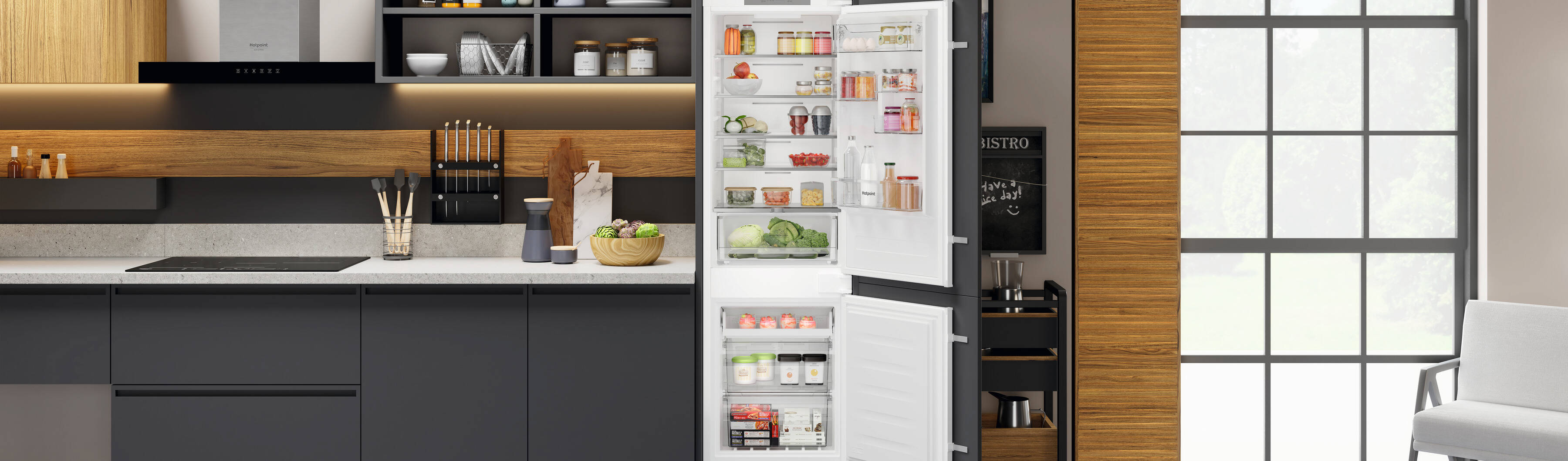 A modern kitchen with dark cabinets, wood accents, and an open fridge stocked with food. The space features a large window, skylights, and open shelving with dishes