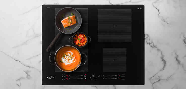 Crna indukcijska ploča na kojoj su 3 lonca različite veličine. U njima se peče losos, kuha juha od bundeve i dinsta mrkva.